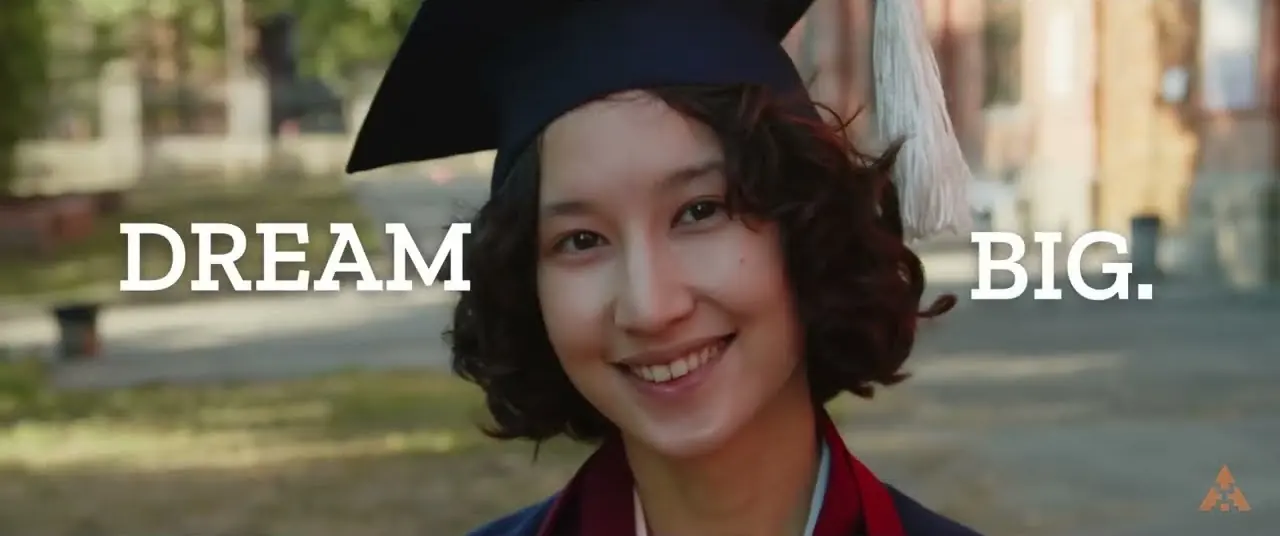 A graduate in a cap smiles between the words Dream and Big, a still from the Women Who Dream film